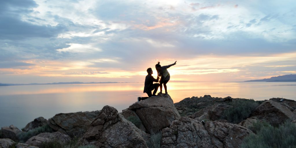 Silhouette of man one knee proposing to woman with ocean background