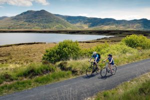 Two people cycling alongside lake